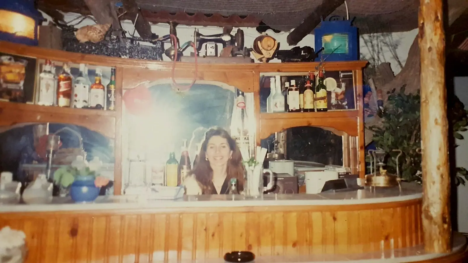 The wooden bar of Snack Bar Paradise in the 1990s, with bottles on the shelves, old lanterns and an antique sewing machine on top