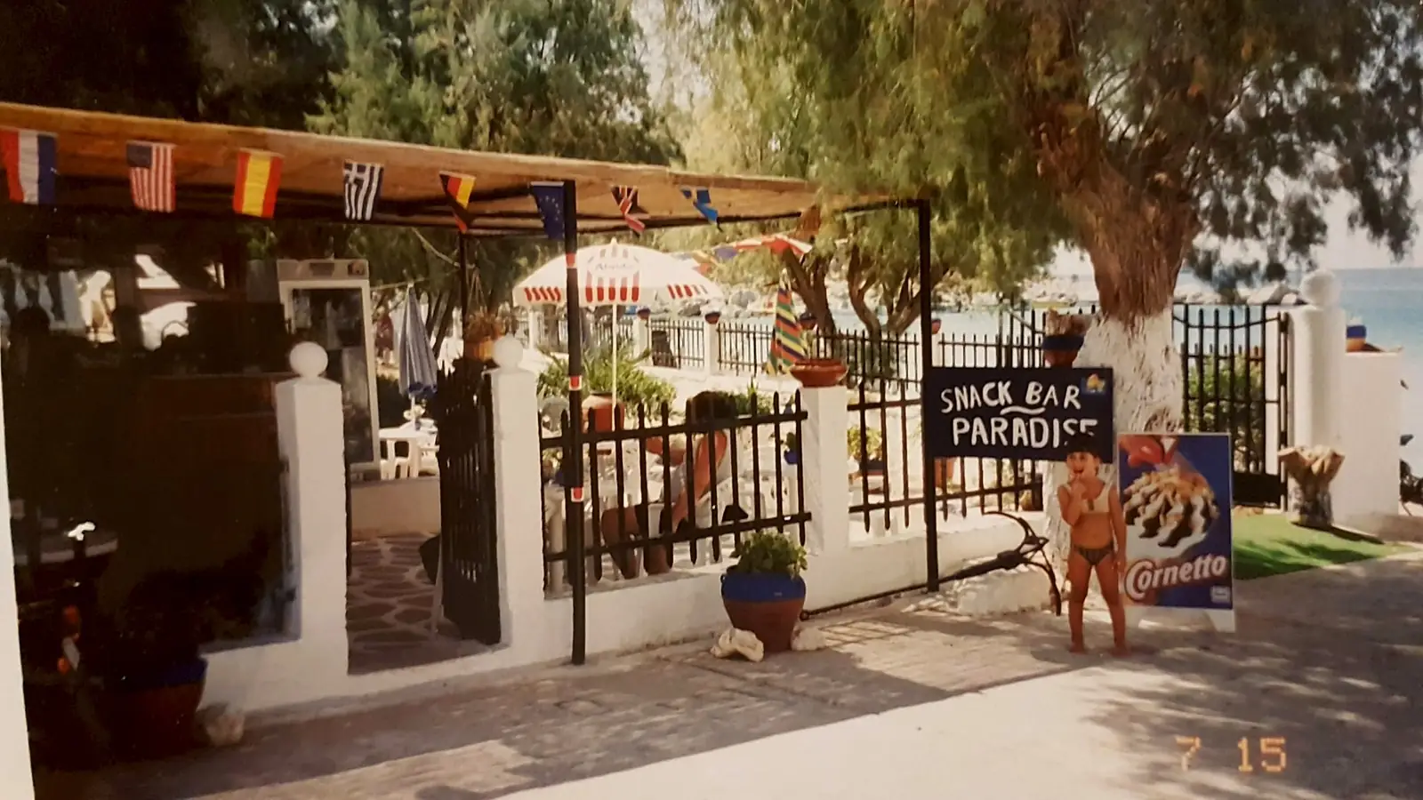 The entrance of Snack Bar Paradise on Vlychadia beach, Kalymnos, in July 1995, with flags on the reed roof and the sea behind